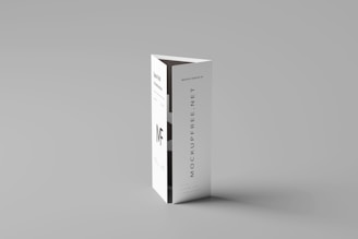 A folded paper brochure with a minimalist design is placed upright against a neutral background. The brochure has text elements, including a bold 'MF' logo and vertical text 'MOCKUPFREE.NET.'