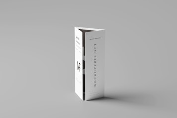 A folded paper brochure with a minimalist design is placed upright against a neutral background. The brochure has text elements, including a bold 'MF' logo and vertical text 'MOCKUPFREE.NET.'