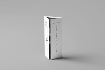 A folded paper brochure with a minimalist design is placed upright against a neutral background. The brochure has text elements, including a bold 'MF' logo and vertical text 'MOCKUPFREE.NET.'