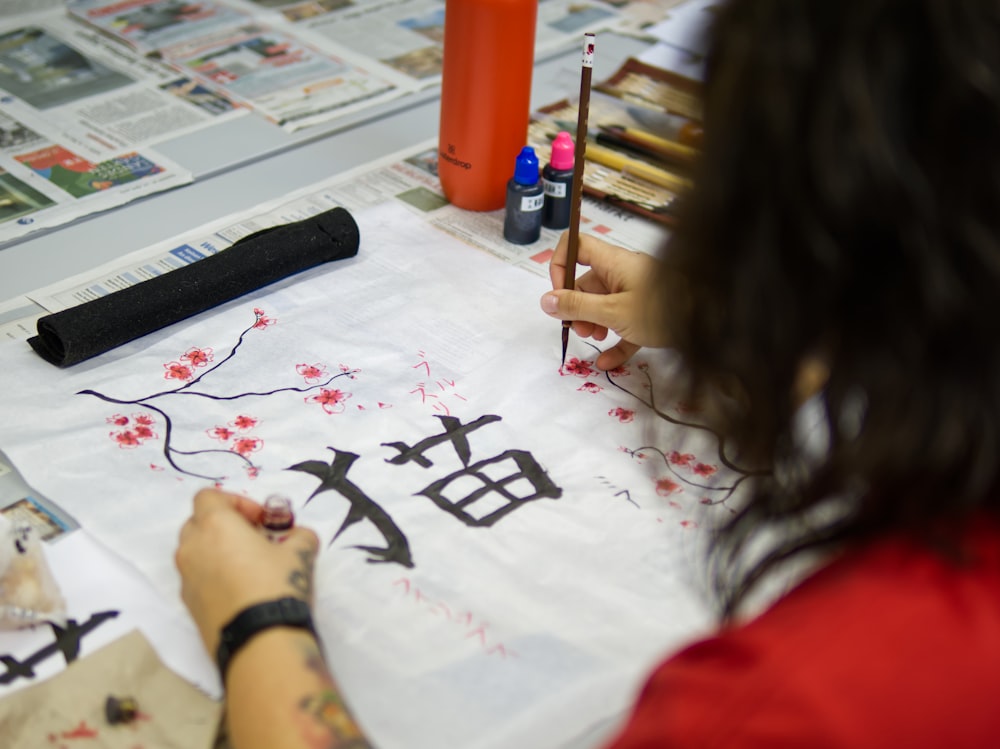 a woman sitting at a table drawing on a piece of paper