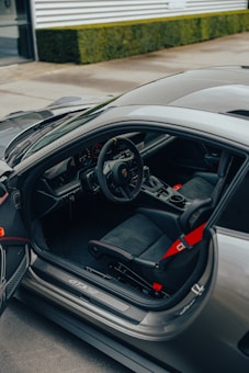 A luxurious car interior with detailed features such as leather seats, a sleek steering wheel, and visible control panel. The car door is open, showcasing the interior design and seating configuration.