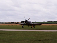 A squadron of vintage fighter planes lined up on an airfield, ready for takeoff under a gray sky.