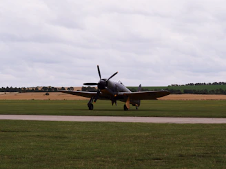 A squadron of vintage fighter planes lined up on an airfield, ready for takeoff under a gray sky.