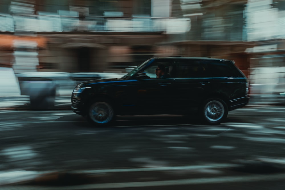 a black suv driving down a street next to tall buildings