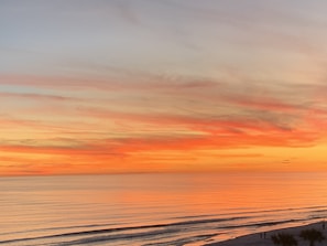 Vibrant sunset over a calm ocean with silhouette of a traveler on the beach