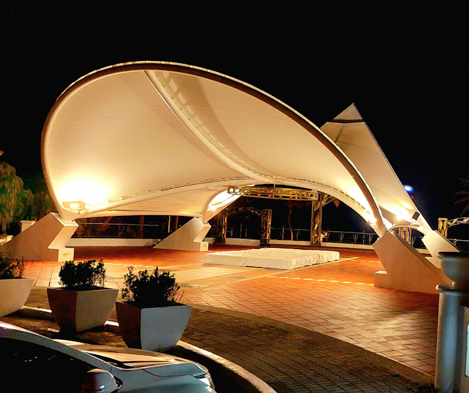 A sleek tensile structure shading a busy commercial parking area under a bright sky.