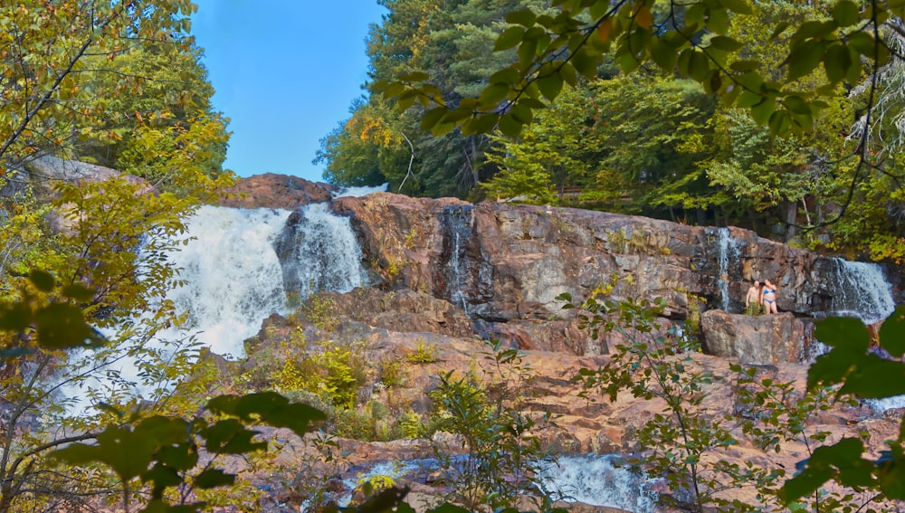 a couple of people standing at the base of a waterfall