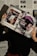 A person holds two magazines in front of their face, obscuring their identity. The left magazine features technology-focused content with a headline for 'Digital Vision' and an image of an e-reader. The right magazine, titled 'foto', shows a close-up of a woman with a short, dark hairstyle. The background consists of more magazine pages or printed text. The lighting casts shadows, creating a dramatic effect.