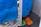 A close-up of a blue towel hanging on a radiator, with a fuzzy mop or cleaning cloth visible behind it. The floor has dark tiles, and a small orange and green object can be seen in the corner.