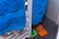 A close-up of a blue towel hanging on a radiator, with a fuzzy mop or cleaning cloth visible behind it. The floor has dark tiles, and a small orange and green object can be seen in the corner.