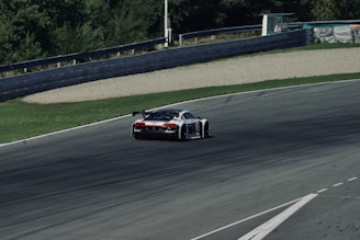 A sleek race car speeds along a curved asphalt track surrounded by greenery. The car features a sporty design with aerodynamic features and sponsorship decals. It is positioned towards the upper center of the image, leaning into the curve.
