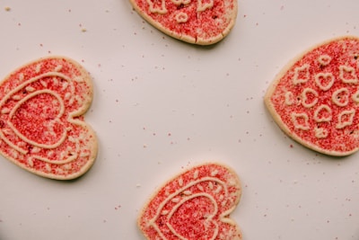 Close-up of heart-shaped dog treats decorated with pink icing and sprinkles on a rustic wooden board.