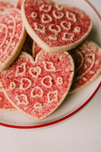 Close-up of heart-shaped dog treats decorated with pink and red icing on a rustic wooden table.