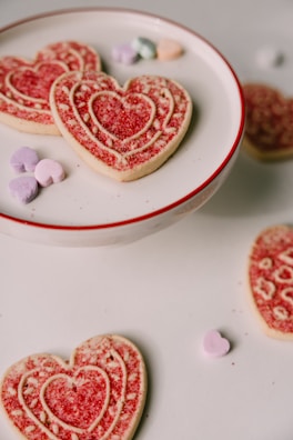 Freshly baked cookies with pastel icing shaped like hearts and stars on a vintage ceramic plate.