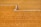 A person is working on a large expanse of spread grain, using a tool to rake the surface, creating patterns in the golden grains. The setting appears to be outdoors, with the ground entirely covered in the dry grains, which are likely being dried in the sun.