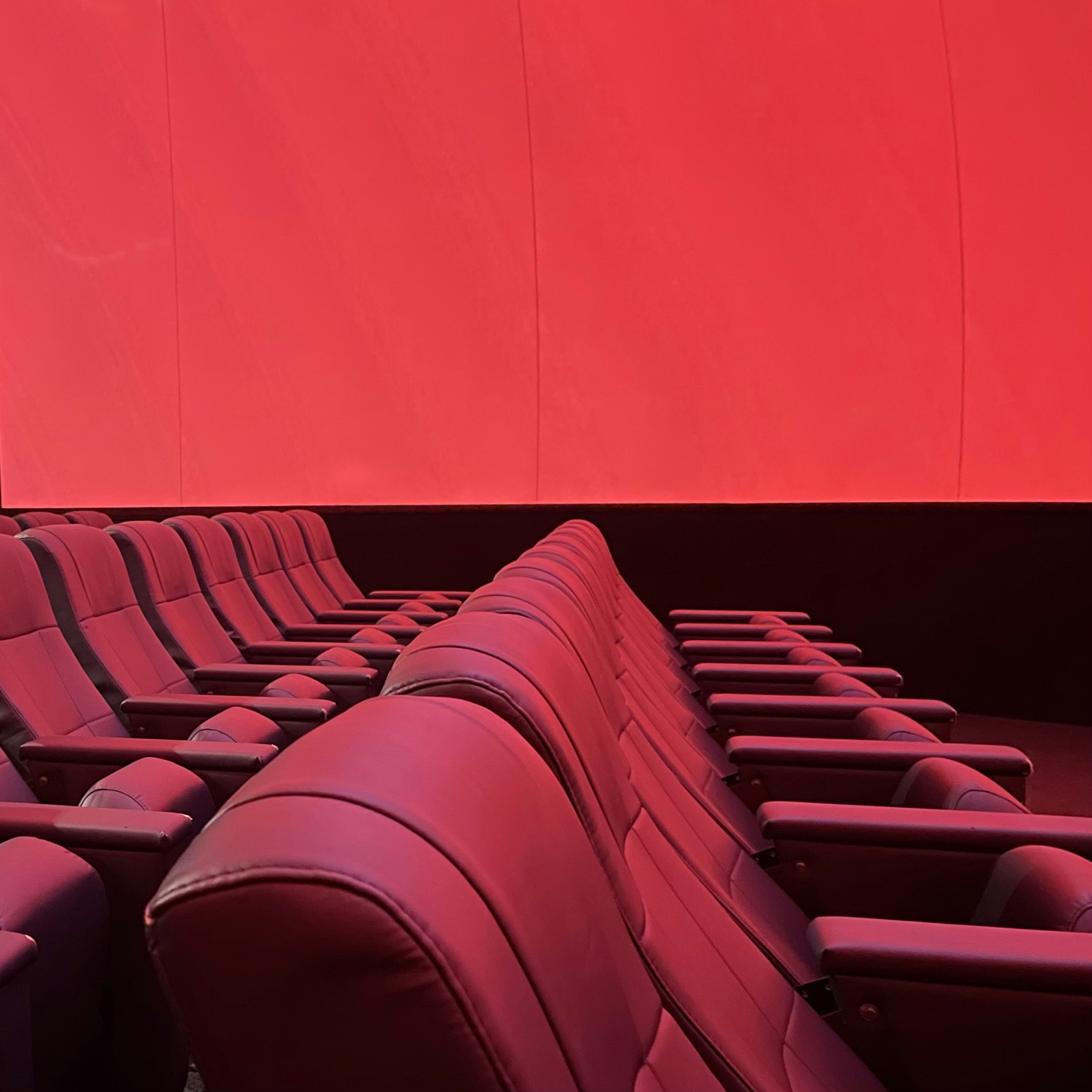 Cinema screening room with rows of seats facing a bright projector screen, warm atmospheric lighting