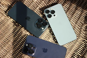 three iphones sitting next to each other on a wicker surface
