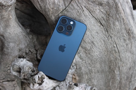 A smartphone with a blue back and multiple camera lenses rests against a textured piece of driftwood, creating a contrast between technology and nature.