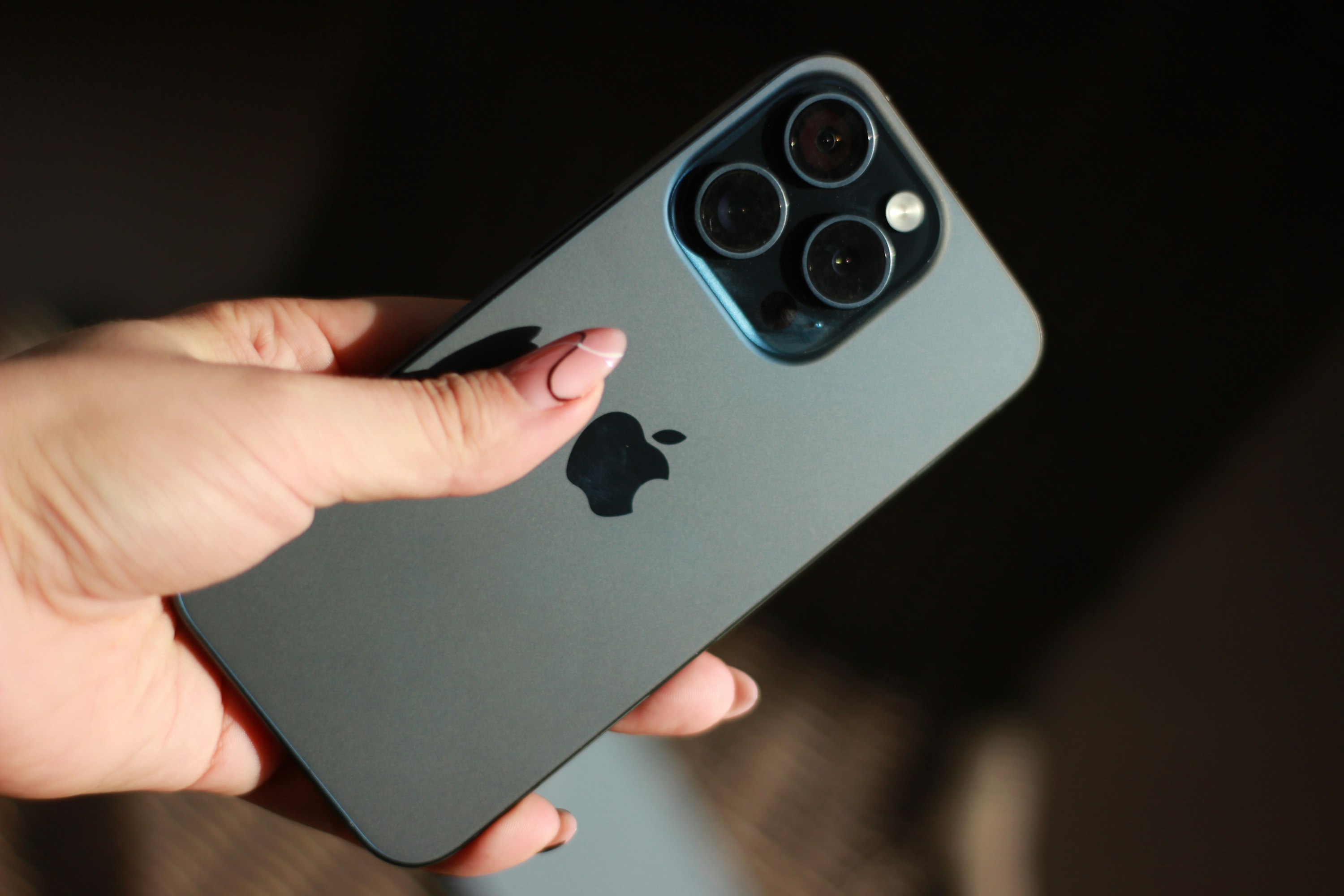 Mão esquerda com as unhas pintadas a segurar um iPhone virado de costas.