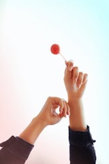 Two hands are raised against a gradient background; one is holding a red lollipop.