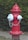 A red fire hydrant is situated on a grassy area next to a sidewalk, surrounded by lush green foliage. The hydrant has two silver caps and a chain connecting them.
