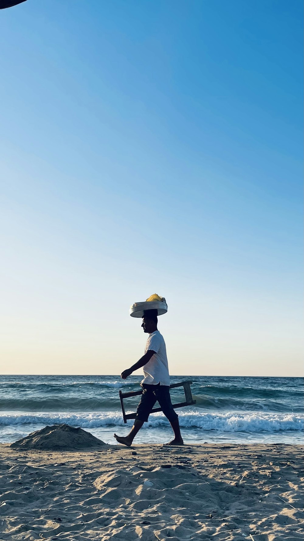 a man walking on the beach carrying a tray of food on his head