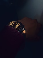 Artistic shot of a wrist wearing a dark, refined watch with soft shadows and noir aesthetic.