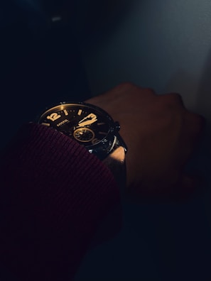 Artistic shot of a wrist wearing a dark, refined watch with soft shadows and noir aesthetic.