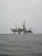 An offshore oil rig is situated in the middle of the sea, with multiple cranes and a complex structure made up of platforms and supports. The surrounding water appears calm, and the sky is overcast, giving a sense of isolation and vastness.