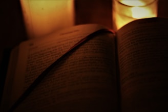 An open antique book with flickering candlelight casting warm shadows.