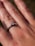 A close-up view of a hand wearing an engagement ring with a single diamond set in a simple metal band. The focus is on the ring finger, highlighting the sparkle of the diamond. The skin texture and lines on the hand are clearly visible.