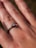 A close-up view of a hand wearing an engagement ring with a single diamond set in a simple metal band. The focus is on the ring finger, highlighting the sparkle of the diamond. The skin texture and lines on the hand are clearly visible.