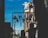 A clothesline with various lingerie items is silhouetted against a bright blue sky. Two figures can be seen in silhouette, one wearing a hat and the other with their hand on their head. The background reveals part of a brick building and a streetlamp, with the words 'Pavo Couture Amsterdam' visible on the window glass.