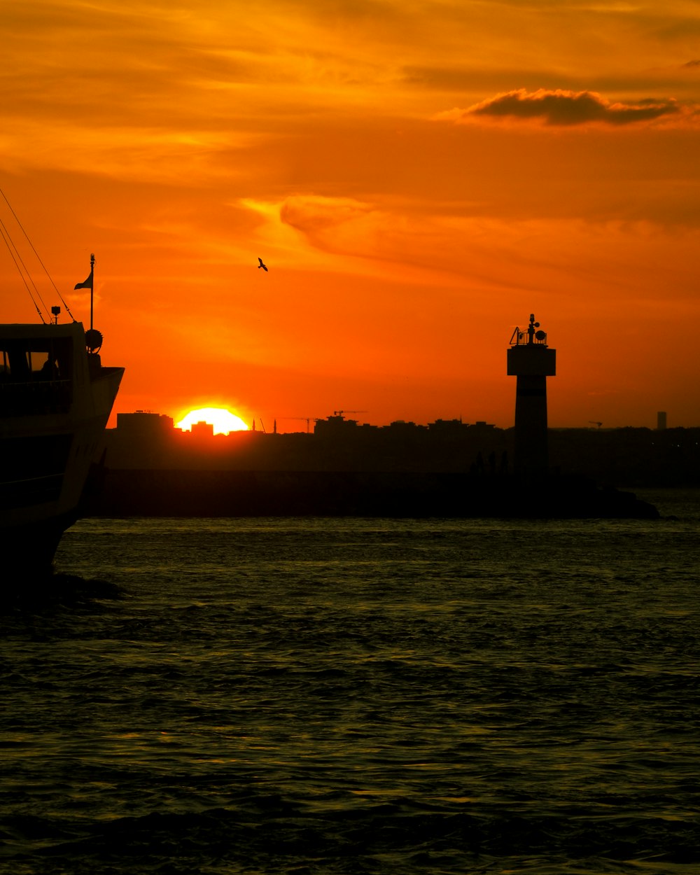 a boat in the water at sunset with a lighthouse in the background