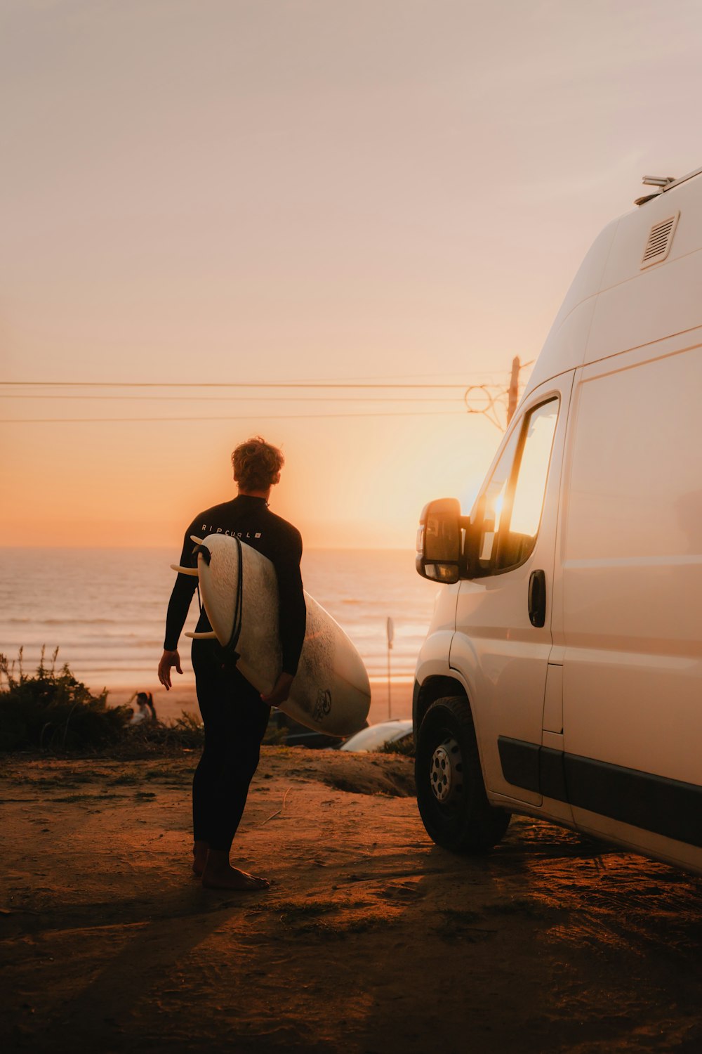 a man carrying a surfboard next to a van