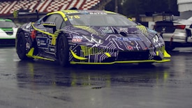 A race car with a futuristic design featuring circuit board patterns and vibrant accents of yellow and blue. The vehicle is parked on a wet, reflective surface, surrounded by other racing cars in the background.