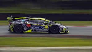 A modern supercar wrapped in a striking black and neon green design, captured in motion.