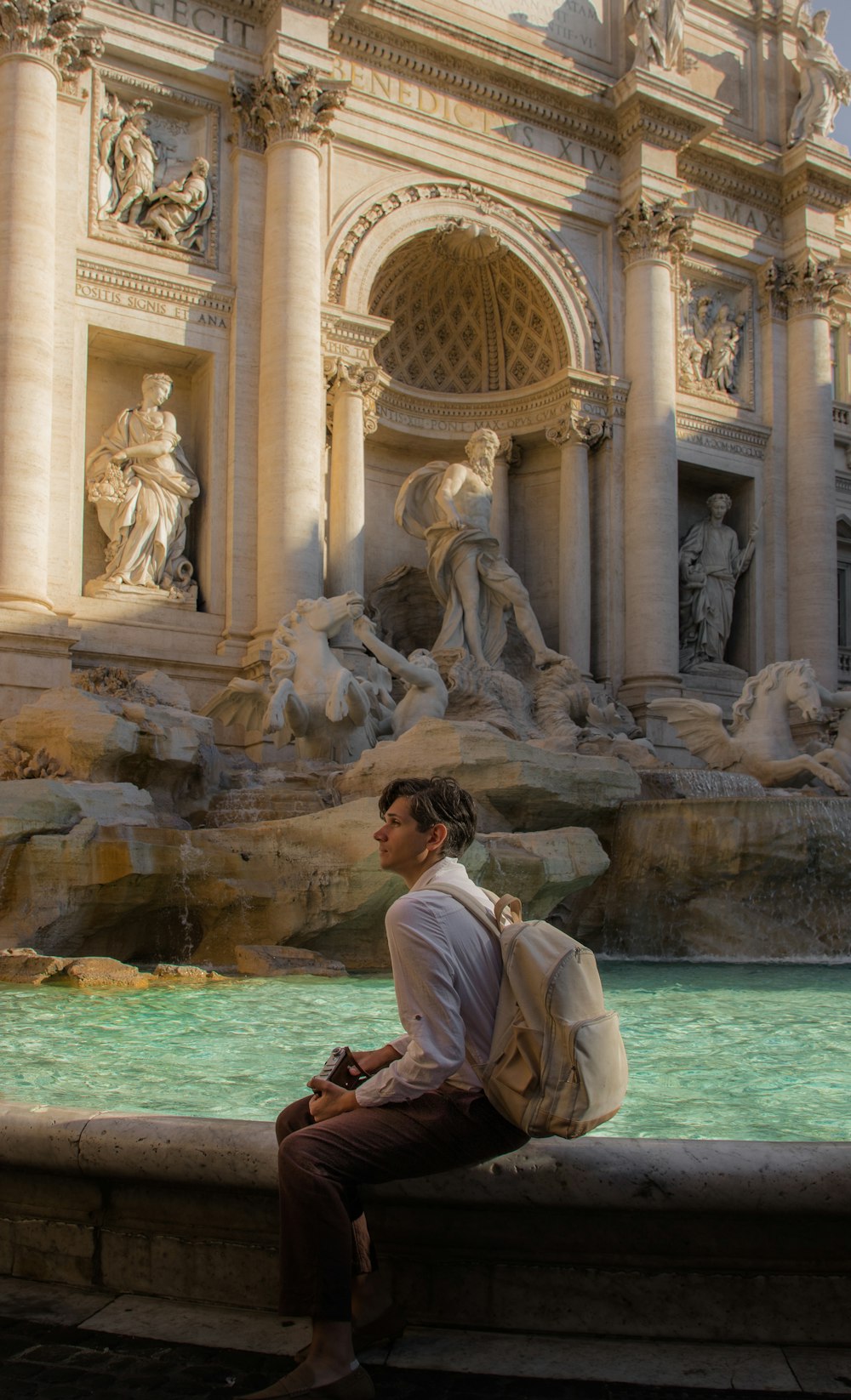 a man sitting on a ledge in front of a fountain