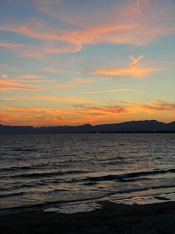 Sunset view over a serene Balinese beach with soft orange and blue ocean hues.
