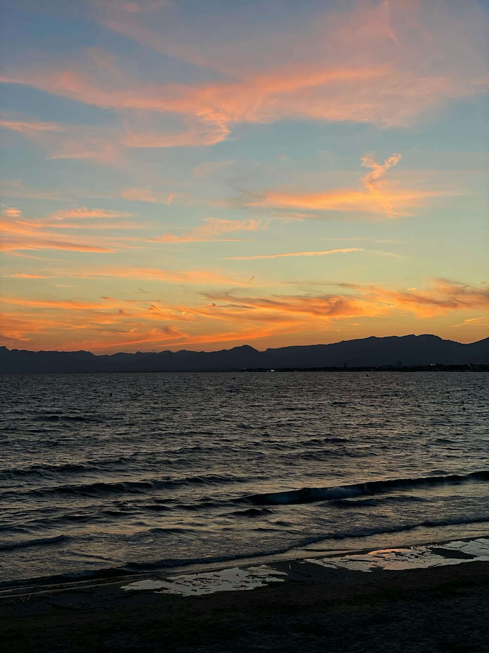 the sun is setting over the ocean with mountains in the distance