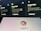 The image shows a blurred background with displays of Google services such as Google Flights, Google Hotels, and Google Maps. In the foreground, there is a clear view of a screen displaying the Copilot logo with colorful overlapping shapes.