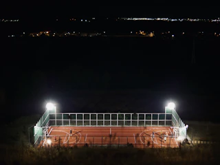 Elegant nighttime shot featuring sport court lighting illuminating a fenced court.