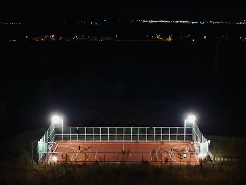Elegant nighttime shot featuring sport court lighting illuminating a fenced court.