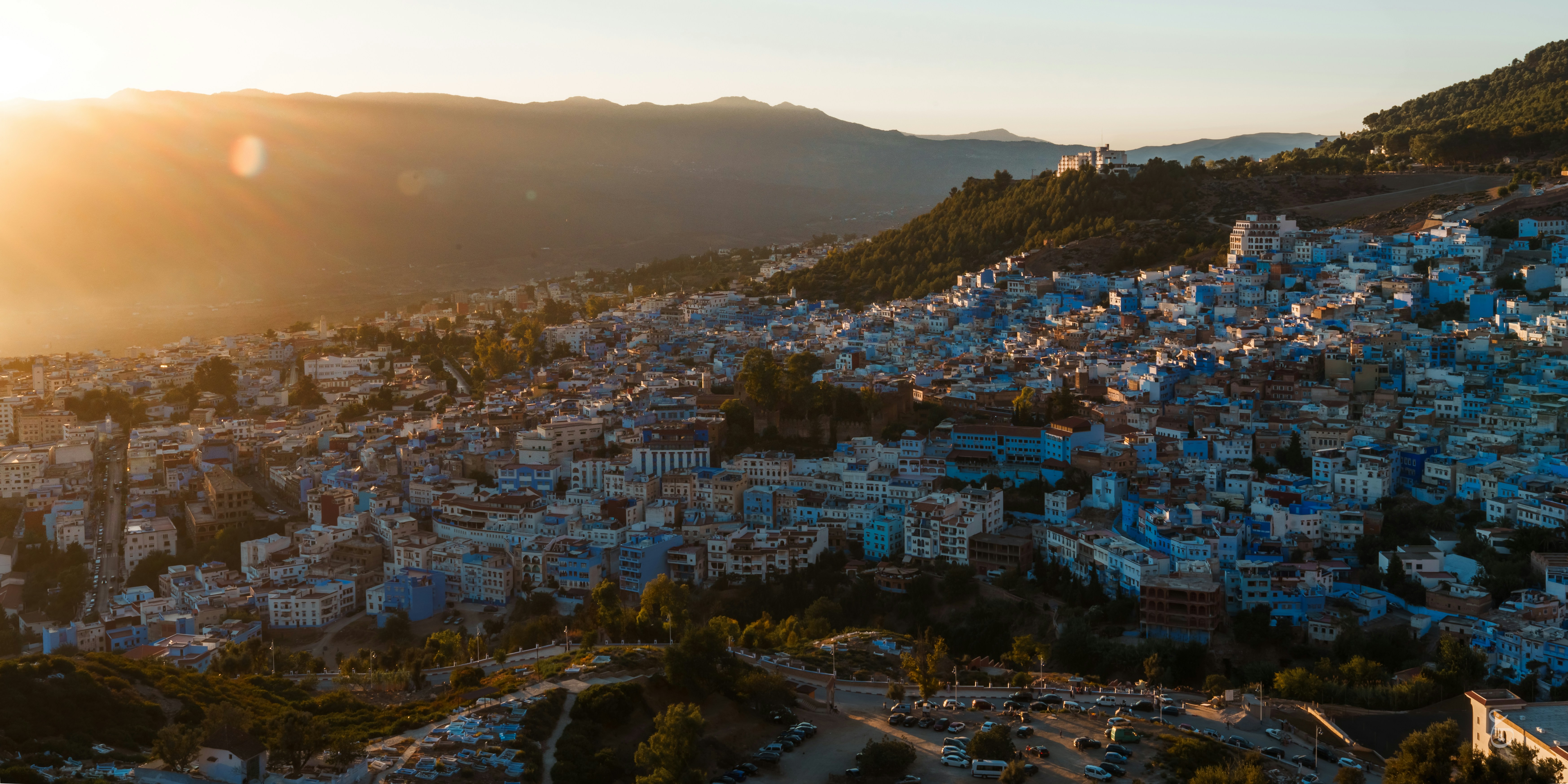 a view of a city with mountains in the background, the blue city during the golden hour.