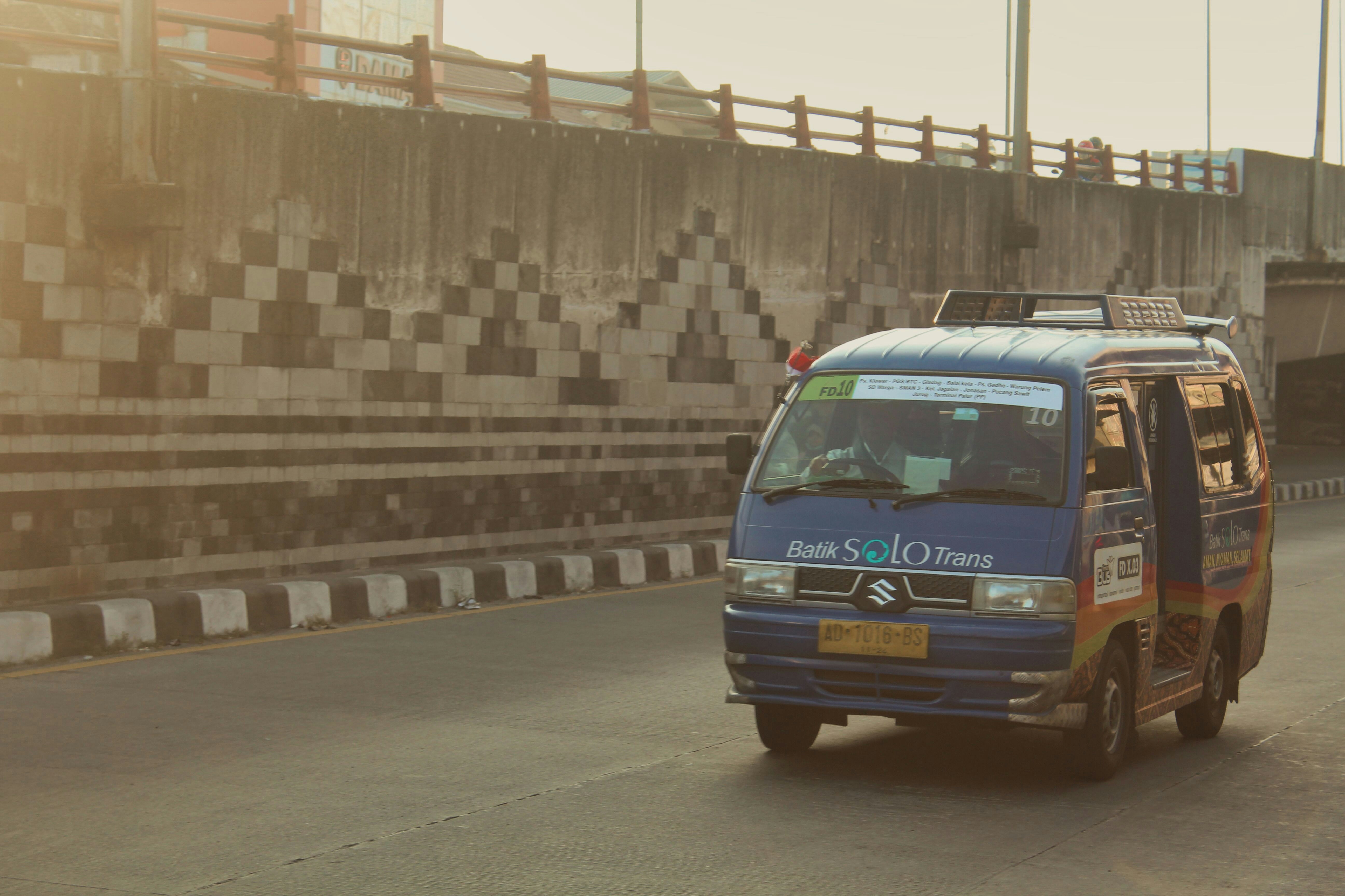 a blue van driving down a street next to a bridge