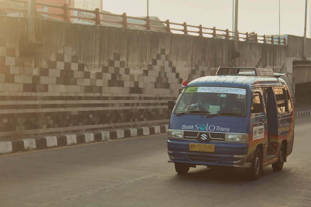 a blue van driving down a street next to a bridge