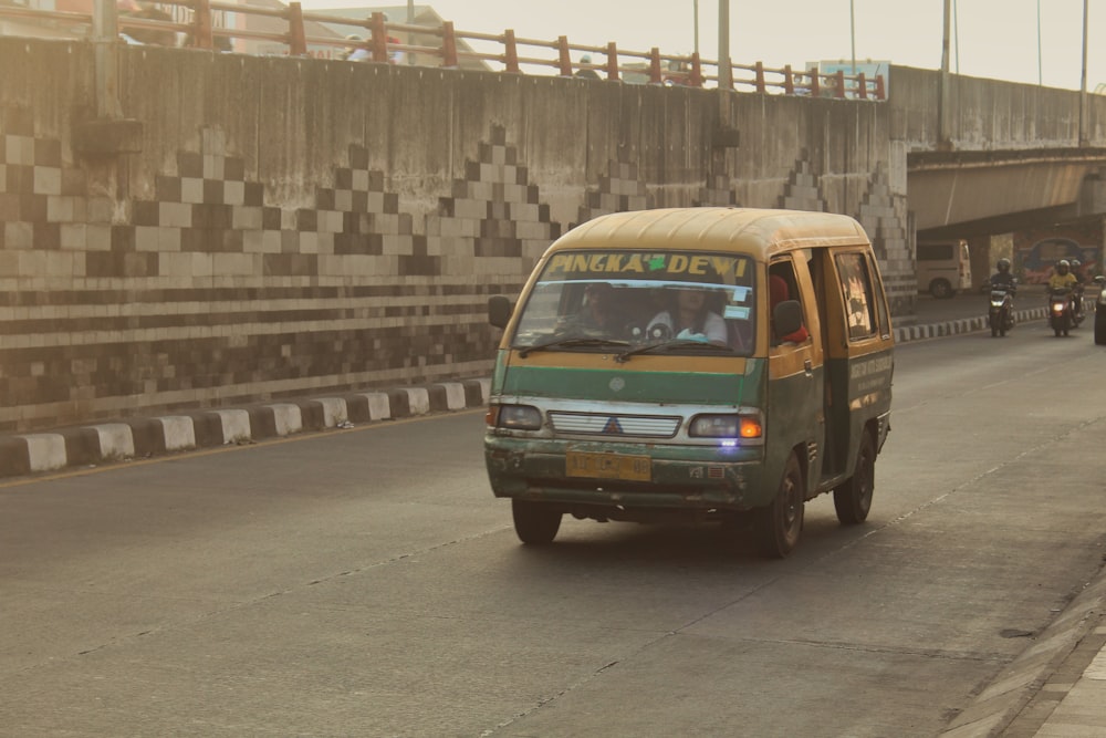 a green van driving down a street next to a bridge