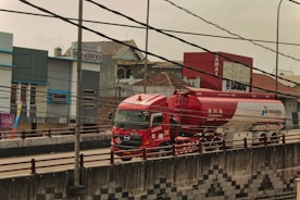 a red truck driving down a street next to a tall building