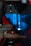 A close-up of industrial machinery with metallic components, featuring a combination of mechanical arms and a sleek, angular design. The background is infused with a bright blue light, contrasting with darker shadows and red accents.