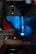 A close-up of industrial machinery with metallic components, featuring a combination of mechanical arms and a sleek, angular design. The background is infused with a bright blue light, contrasting with darker shadows and red accents.